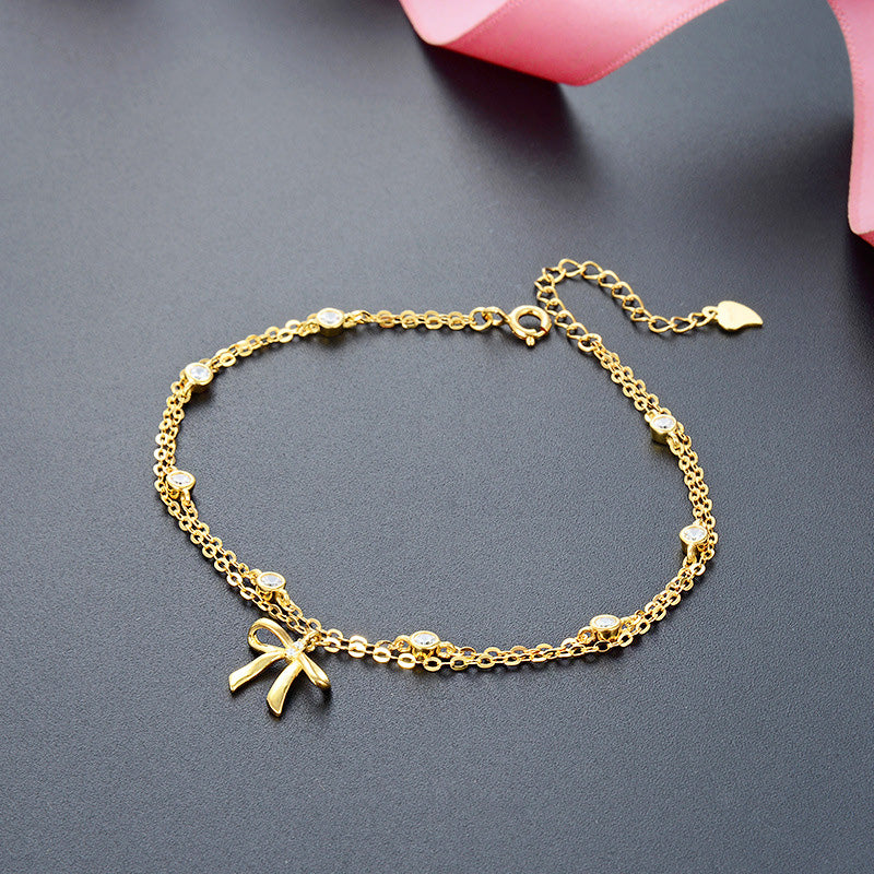 Close-up of a 925 sterling silver, gold-plated two-layer chain bracelet featuring an elegant bow charm with clear stones. Part of a set of 5.