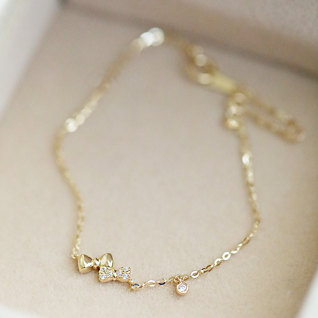 A close-up of a delicate 925 sterling silver chain bracelet, gold-colored, featuring an elegant double bow knot charm with a sparkling central stone.