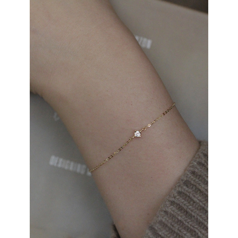A delicate 18k gold-plated S925 silver chain bracelet with a single solitaire cubic zirconia, elegantly worn on a wrist.