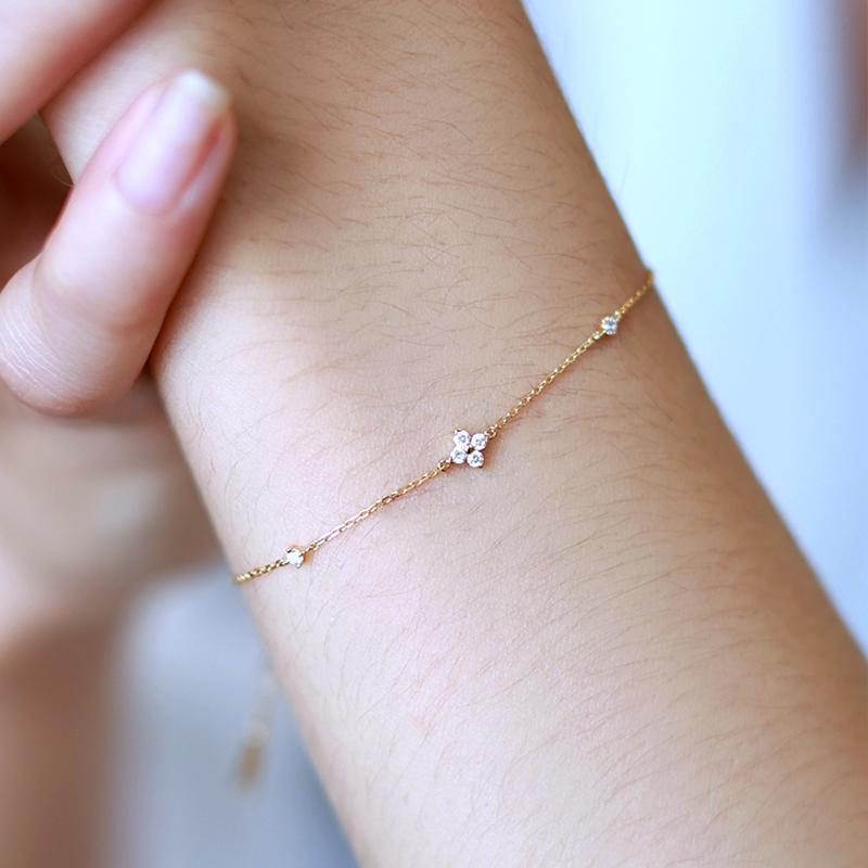 Close-up of a delicate 18K gold-plated sterling silver bracelet featuring a mini four-petal flower charm with a sparkling cubic zirconia center, worn on a wrist.