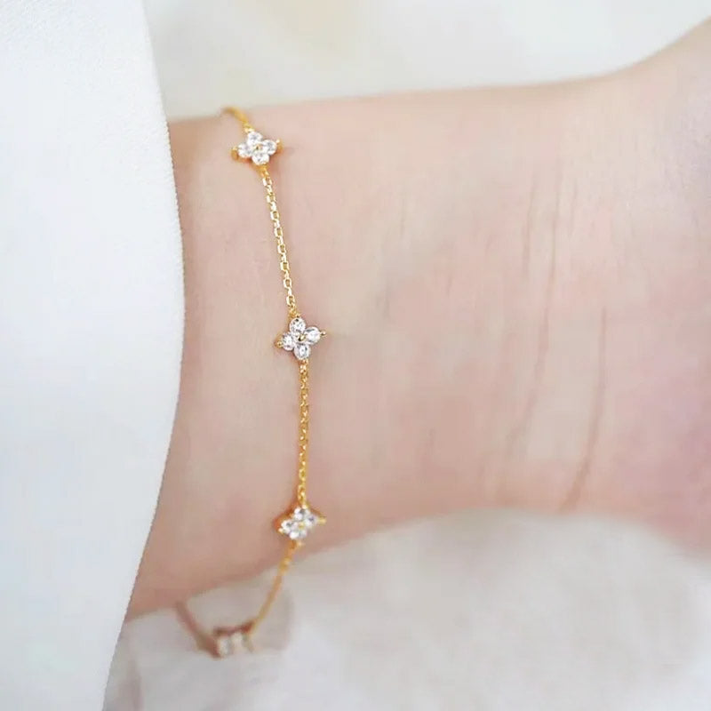 A close-up of an 18k gold-plated 925 sterling silver bracelet from a set, featuring a delicate zircon flower charm.