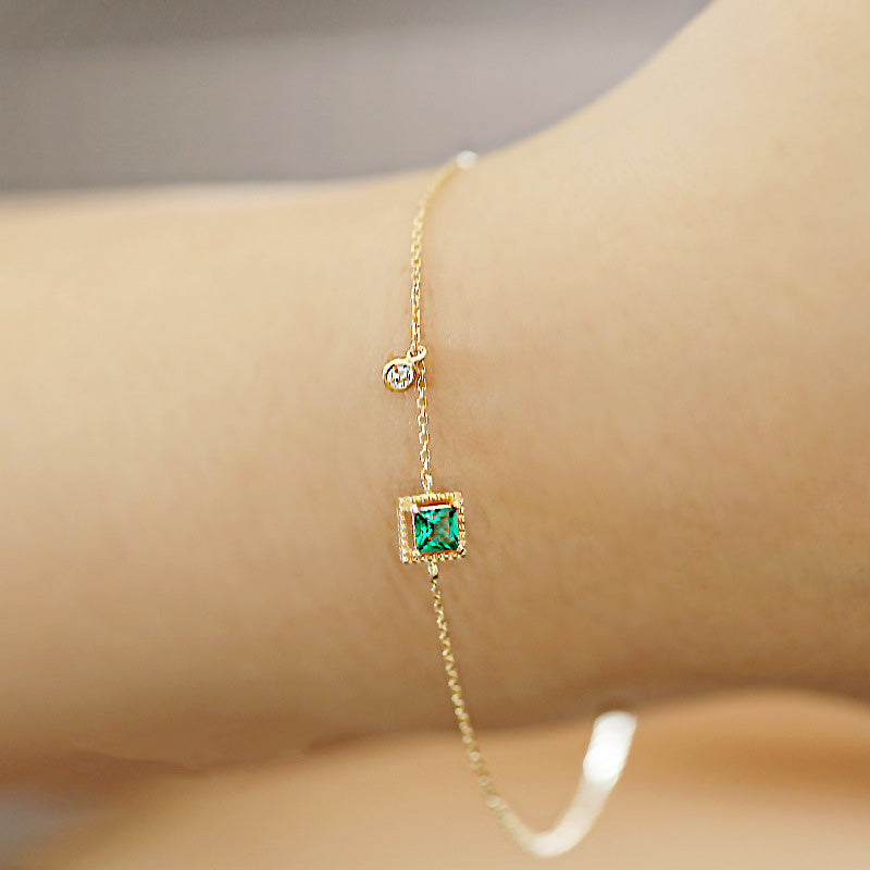 Close-up of a 925 sterling silver gold-plated bracelet featuring a square green emerald zircon and a small clear gemstone.
