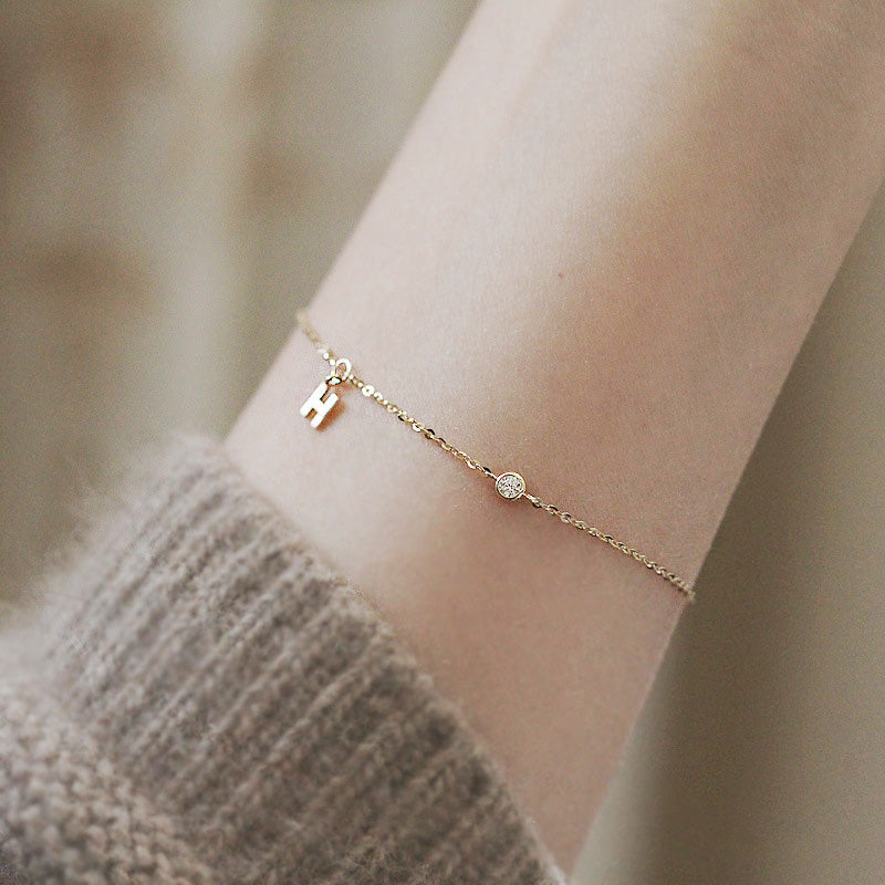 A close-up of a wholesale 925 sterling silver bracelet with a gold finish, featuring a stylish letter 'H' charm and a small sparkling gemstone accent.