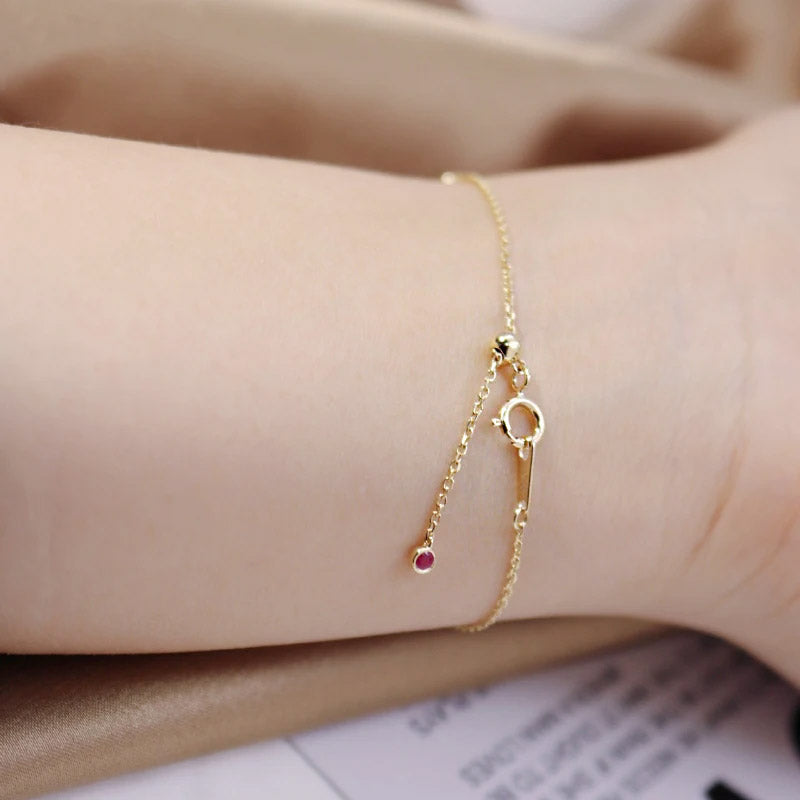 Close-up of a 925 sterling silver chain bracelet with a gold-tone finish, featuring a vibrant round red gemstone charm.