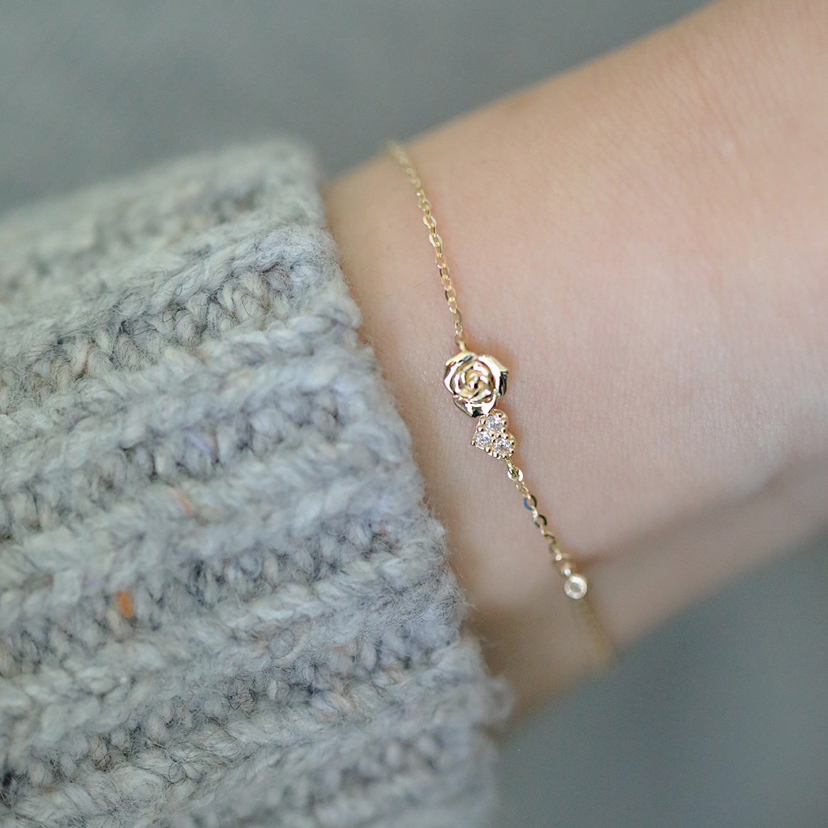 A delicate 925 sterling silver gold-plated bracelet with a tiny rose and a sparkling zirconia heart charm, worn on a wrist.
