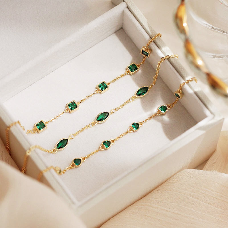 A set of elegant gold-plated 925 sterling silver bracelets with vibrant green emerald-like crystals, displayed in a white jewelry box.
