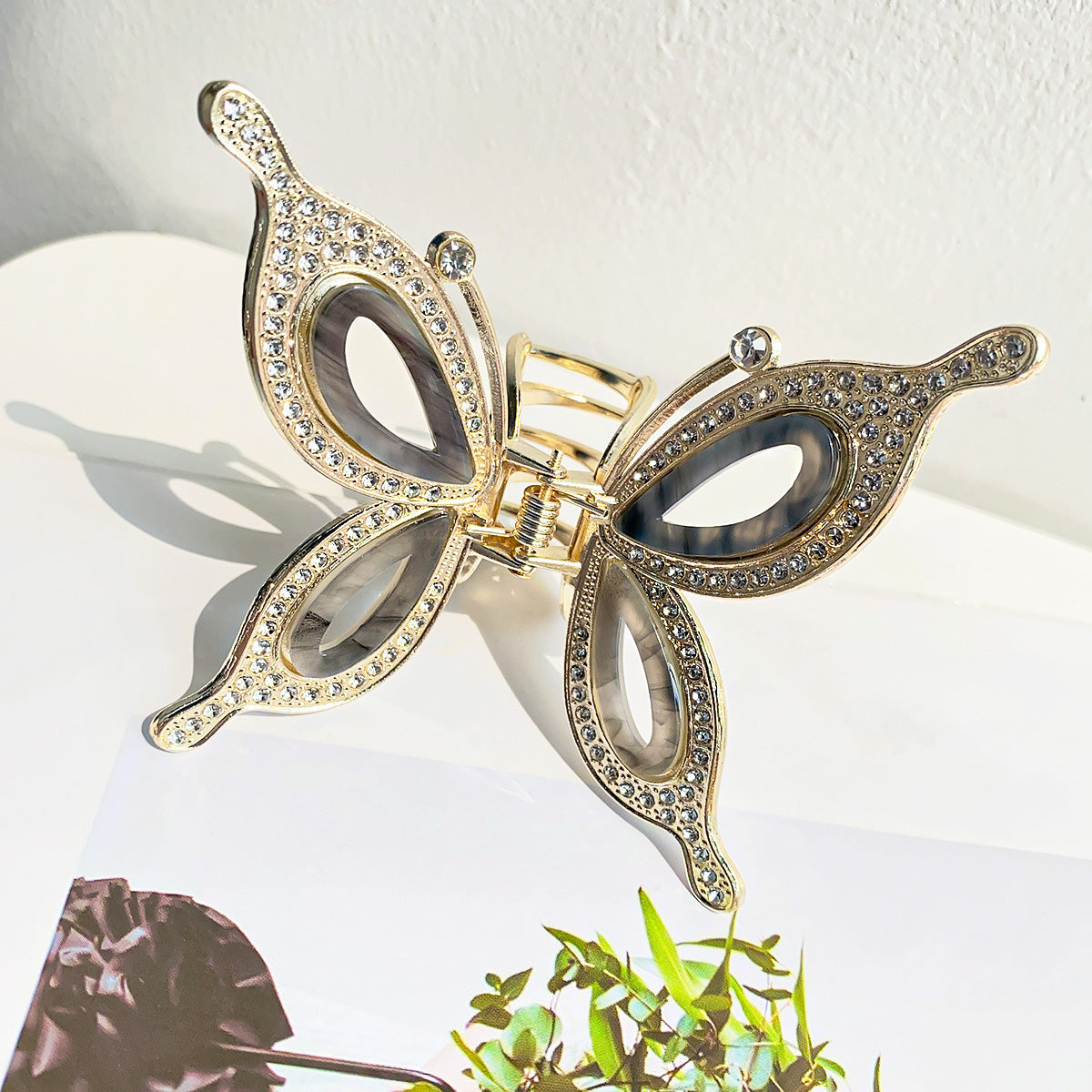 A close-up of a gold metal butterfly hair claw clip, intricately designed with hollowed-out wings and sparkling clear rhinestones.