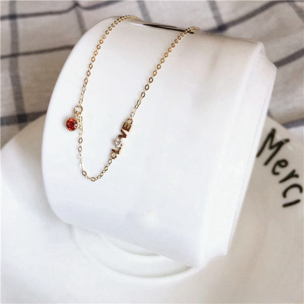 A 14K gold-plated sterling silver necklace featuring a reversible 'LOVE' pendant with a red cubic zirconia, displayed on a white stand.