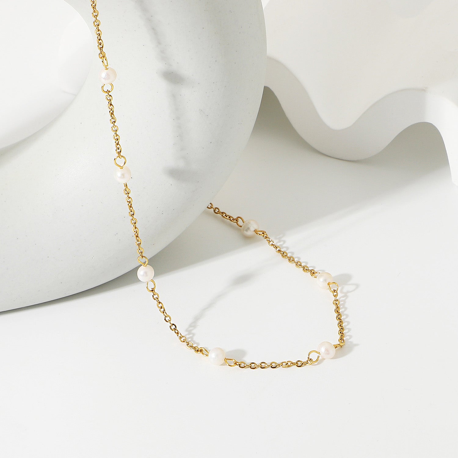 A close-up of the stainless steel gold-plated link chain necklace featuring elegant white pearl charms, displayed on a neutral background.