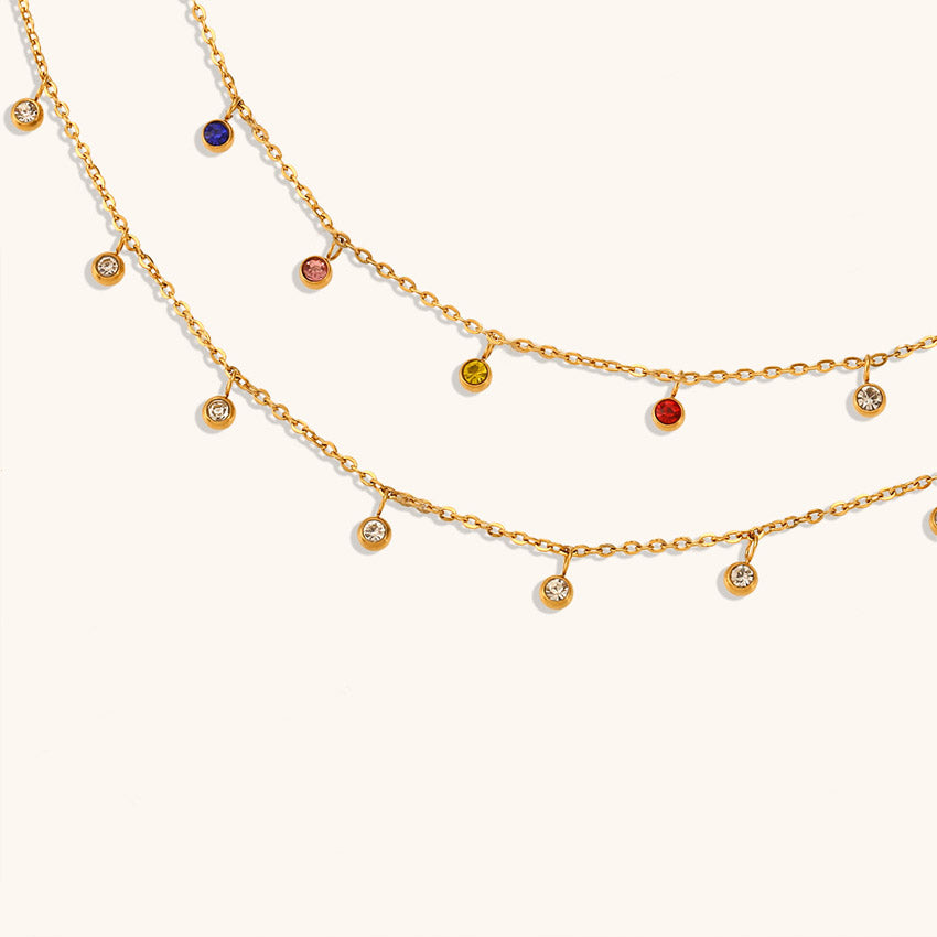 A promotional shot showcasing two stainless steel gold-tone necklaces, one with vibrant multicolour zircon stones and the other with classic white zircon stones.