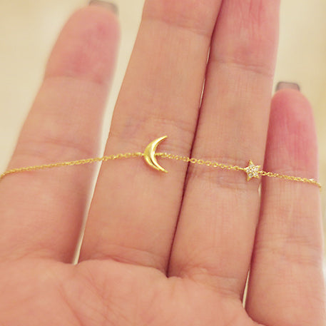 A close-up view of a hand modeling the delicate 925 sterling silver moon and star charm bracelet with a gold finish.