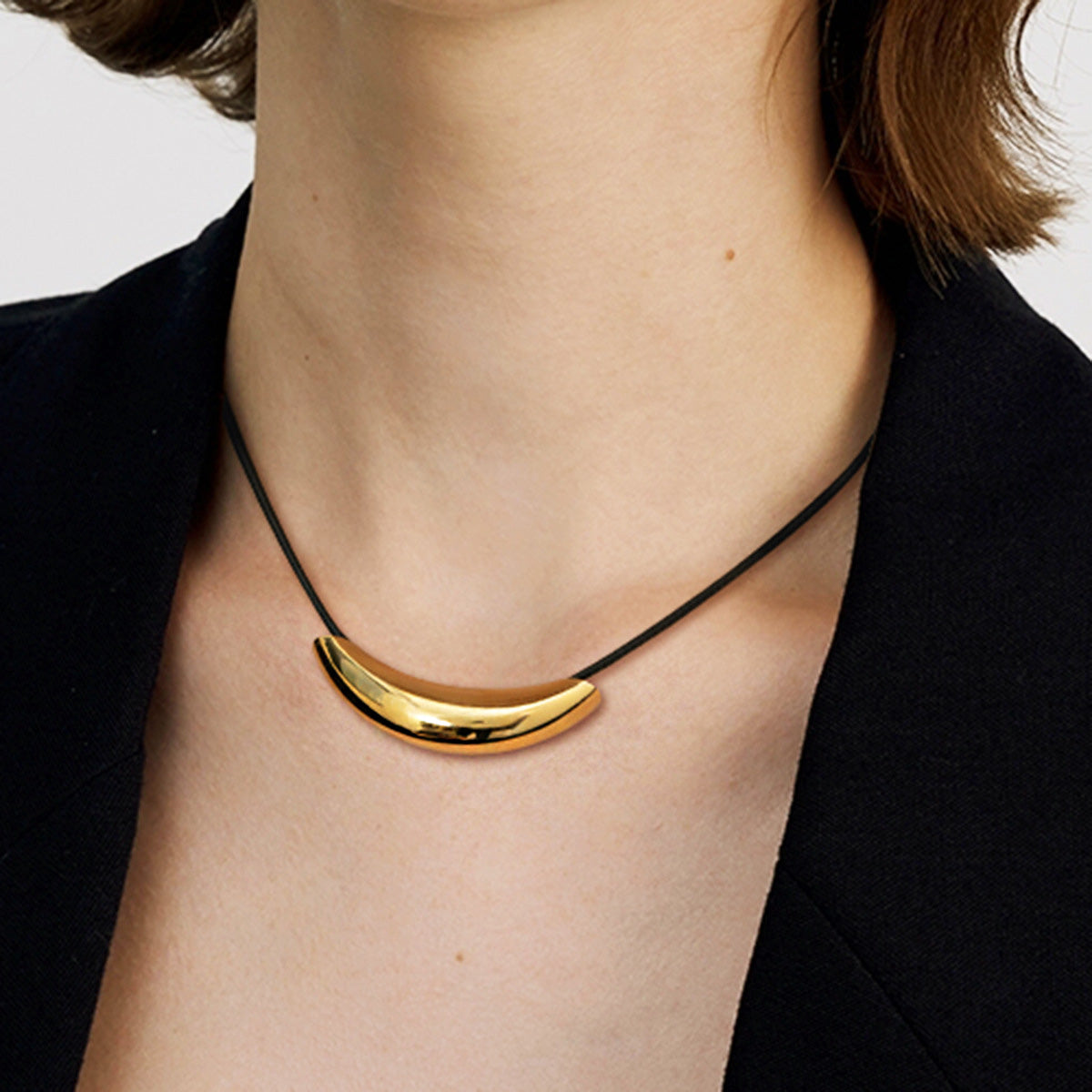A woman wearing a minimalist gold-finish stainless steel crescent charm necklace with a black leather strap.