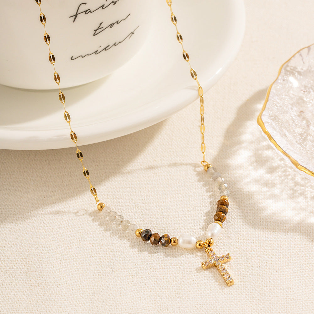 A close-up product shot of a gold-tone stainless steel necklace featuring a delicate beaded chain and a cubic zirconia cross pendant, displayed on a clean white background.