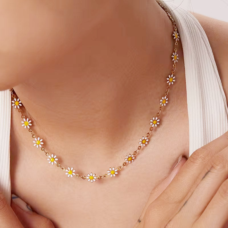 A close-up of a woman wearing a delicate gold chain necklace featuring white and yellow enamel daisy charms, showcasing its elegant look.