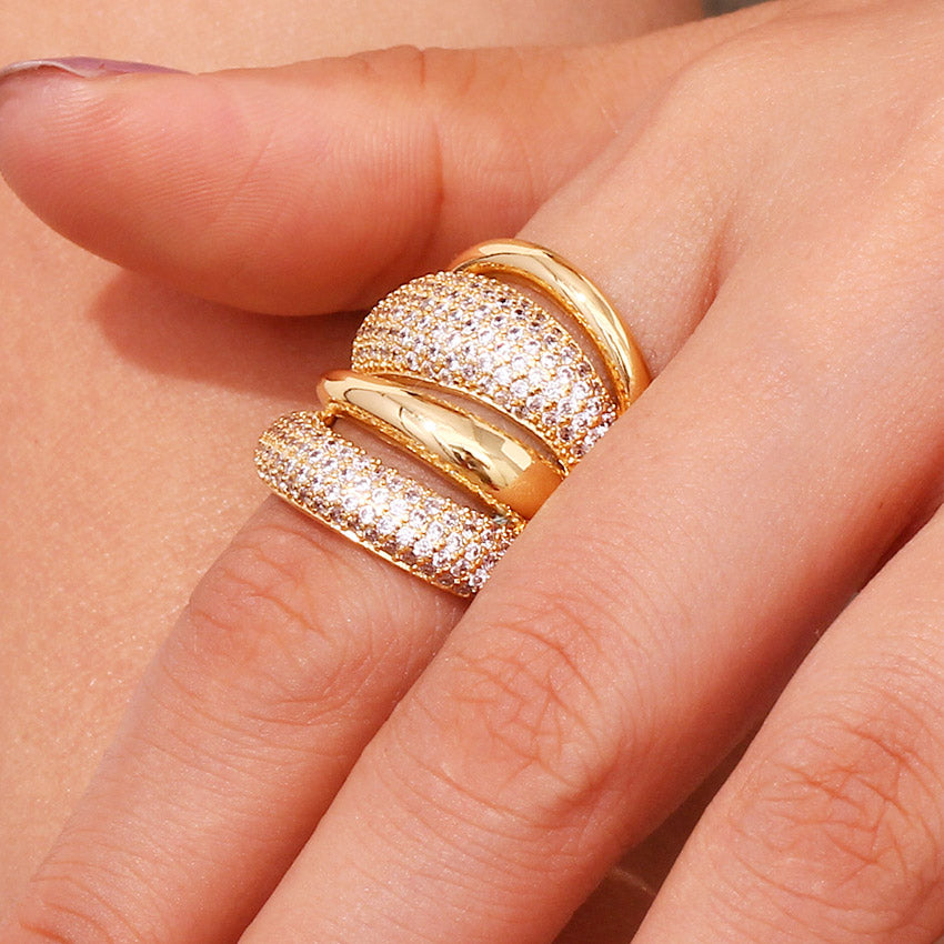 A close-up of a woman's hand wearing a stack of 18K gold plated chunky dome rings, with layers paved in sparkling cubic zirconia.