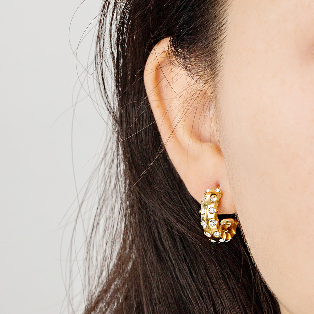 A close-up of a woman wearing the stainless steel gold-inlaid white zirconia C-shape stud earring, showcasing its elegant design and sparkle.