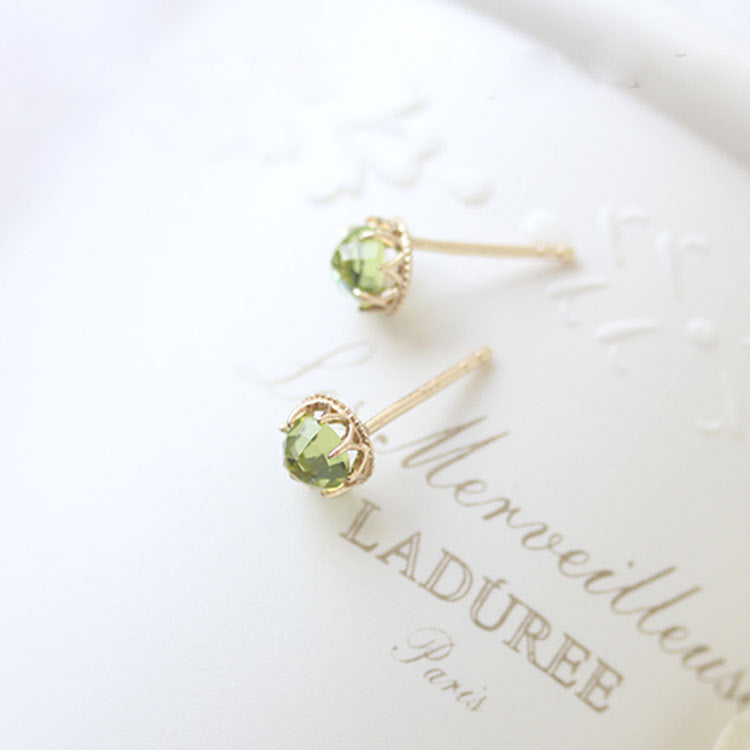 A pair of 925 sterling silver peridot stud earrings with 18K gold plating, elegantly displayed on a white branded box.