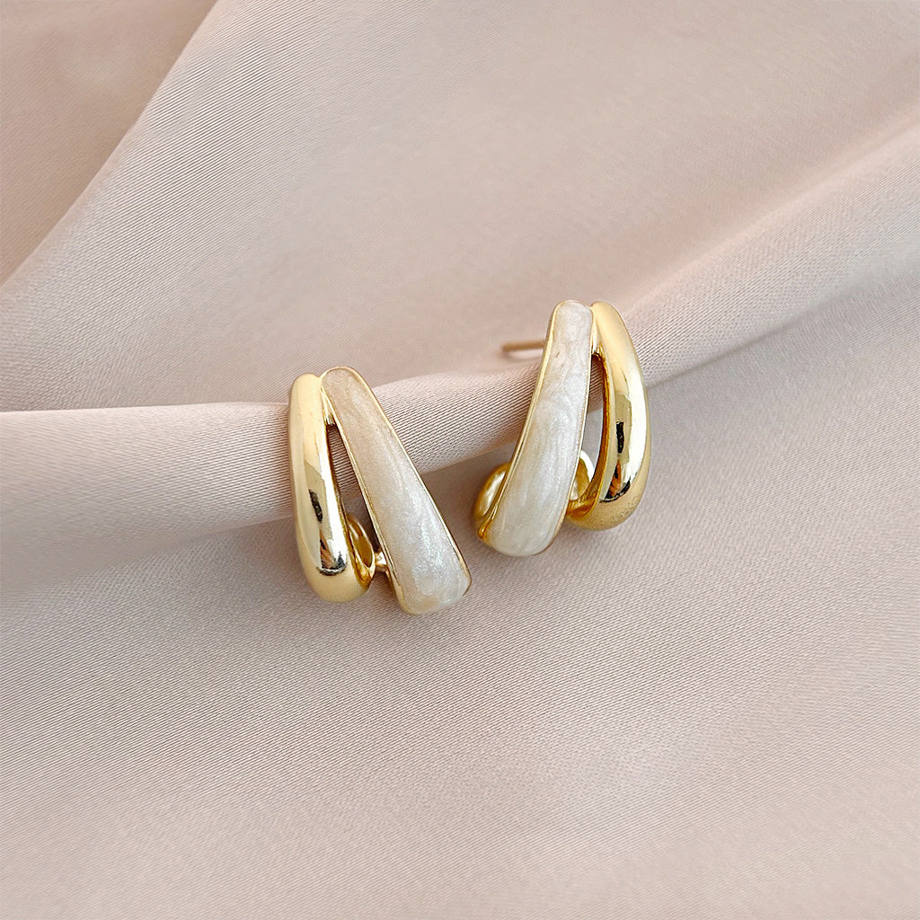 A pair of retro-style 14k gold-plated stud earrings with a twisted, double-layered design and white enamel inlays, on a clean background.
