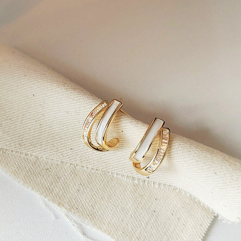 A pair of wholesale 18K gold-plated geometric cross stud earrings with brilliant white enamel inlays and sparkling micro-paved zirconia.