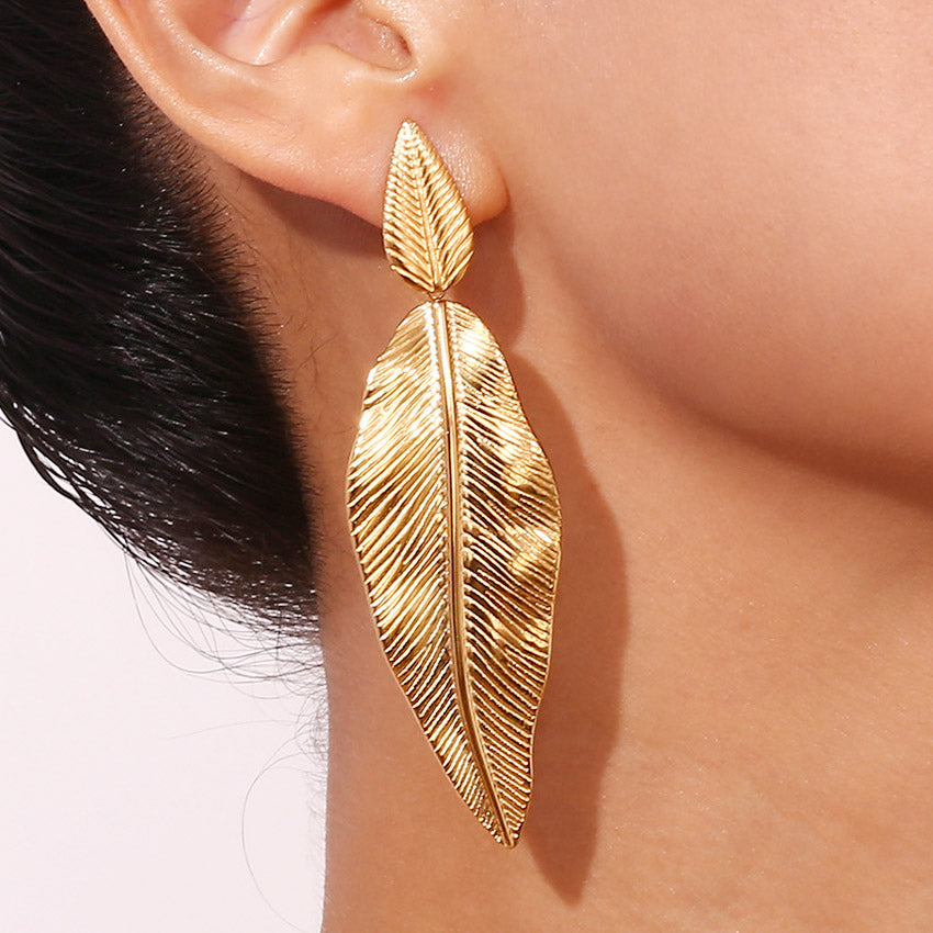 A close-up of a woman wearing a gold-plated stainless steel leaf drop earring, showcasing its bohemian summer style.