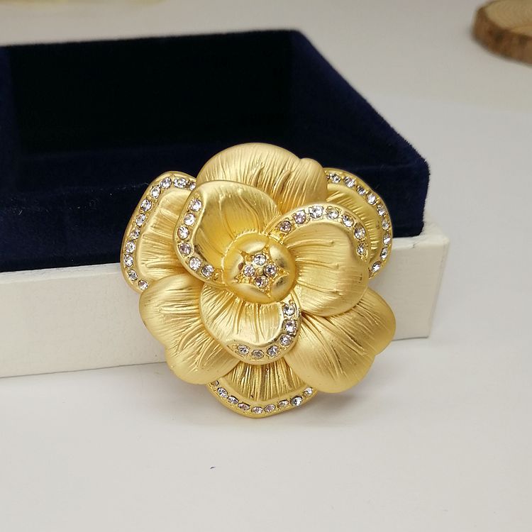 A close-up of the vintage matte gold leaf and camellia brooch, highlighting its intricate flower design and sparkling central rhinestone.