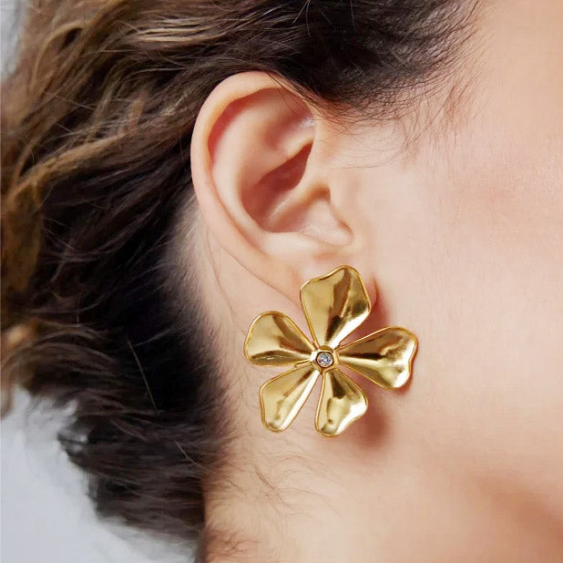 A close-up view of a woman wearing an elegant gold-plated stainless steel big flora flower stud earring, showcasing its detailed design and shine.
