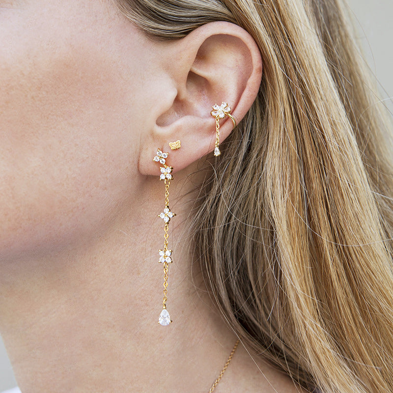 A close-up of a 925 sterling silver long tassel drop earring in a gold finish, featuring an intricate flower design with a dangling chain and a teardrop crystal.
