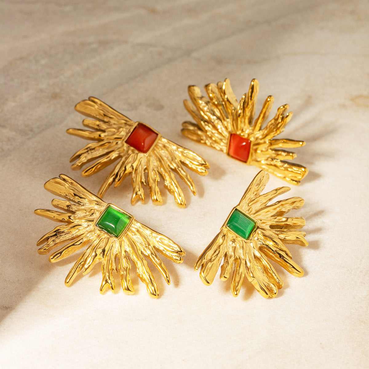 A collection of stainless steel gold-plated drama fan-shaped stud earrings, displaying both the green and red gemstone options on a white background.