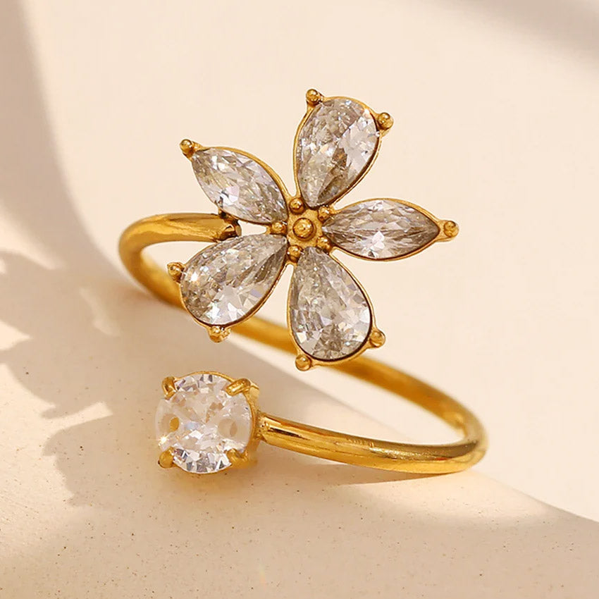 A close-up of an 18K gold-plated stainless steel flower ring with a central clear CZ zirconia stone.
