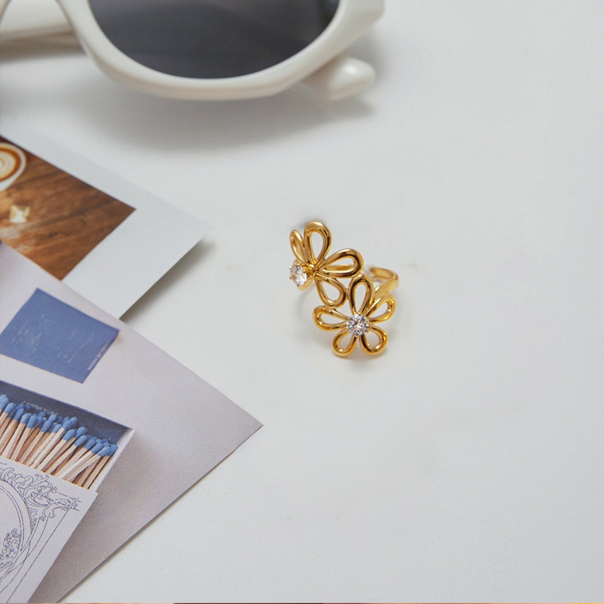 A detailed flat-lay view of the Gold Flower Zircon Ring Set, showcasing the delicate floral design and sparkling zircon stones on a gold-tone titanium steel band.