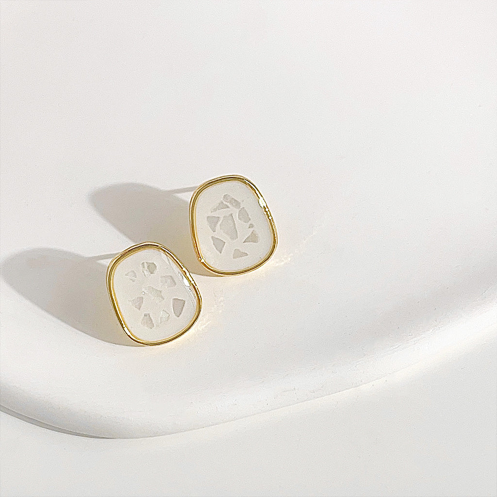 A close-up of the 14k gold plated white enamel rectangle stud earrings, highlighting the delicate shell-like pattern on the white surface.