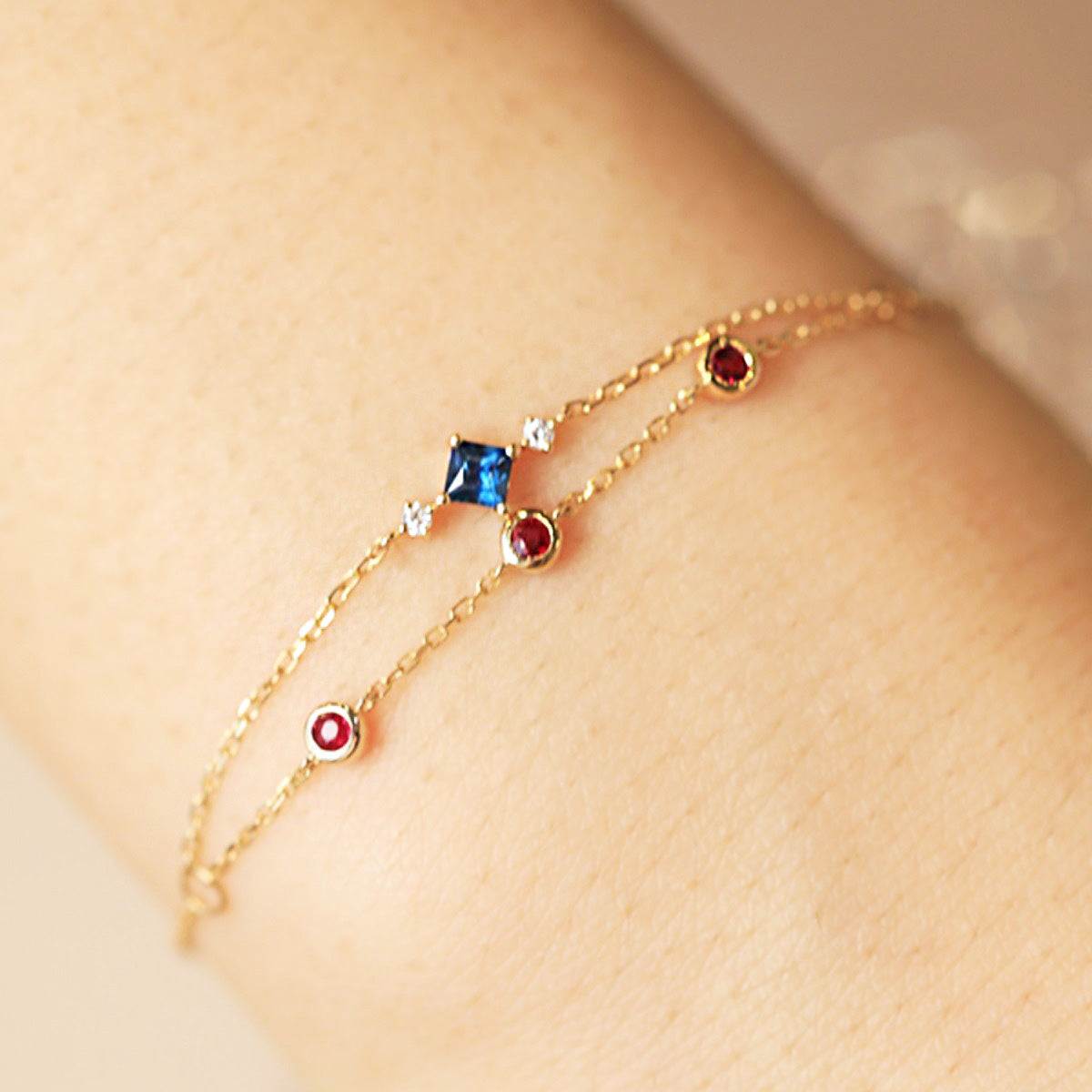 A close-up of a wholesale 925 sterling silver two-layered chain bracelet with colorful blue, red, and white zircon gemstones.