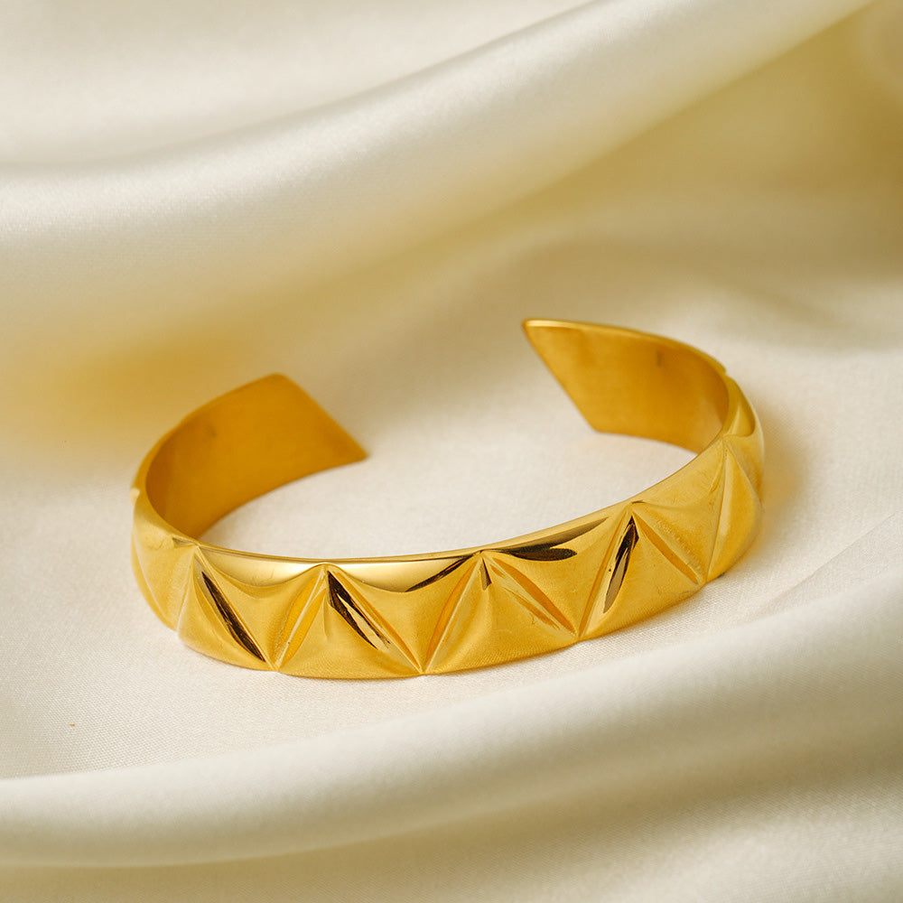 A close-up of the 18K gold-plated stainless steel cuff bracelet, featuring a detailed geometric triangle texture.