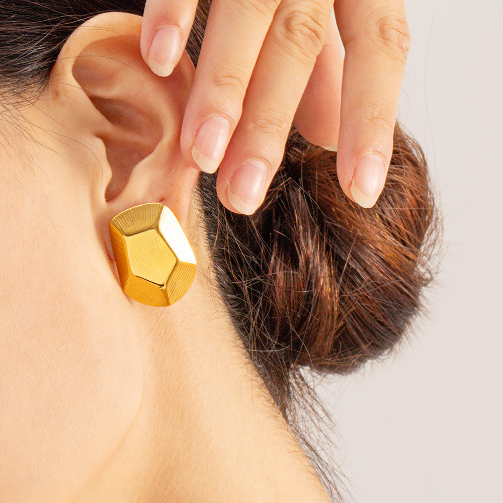 A close-up view of a model wearing the stainless steel geometric striped pentagon stud earring in a gold finish, highlighting its bold design.