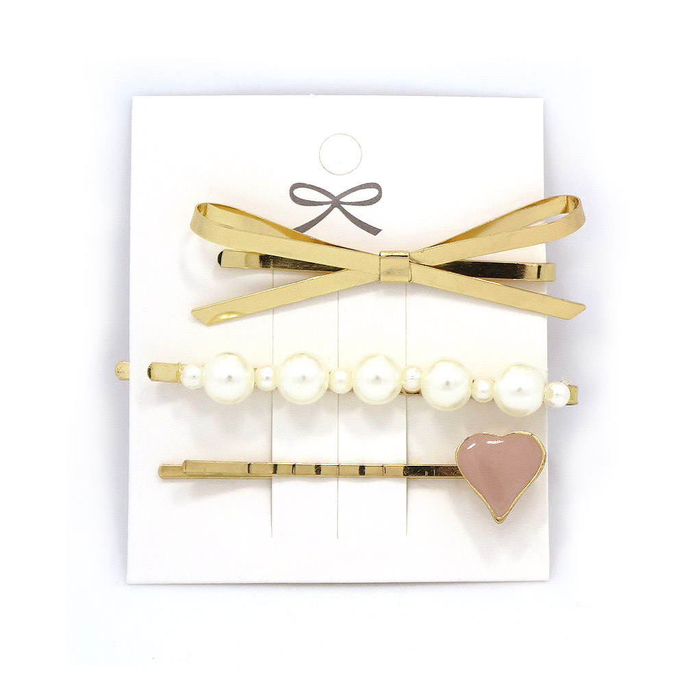 A stylish set of 3 faux pearl and metal hair clips by JR Fashion, featuring a gold bow, a pearl-studded clip, and a pink heart design.