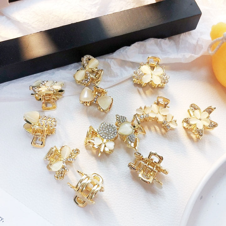 A set of four elegant gold mini hair claw clips, intricately decorated with white opal-like stones and sparkling rhinestones.
