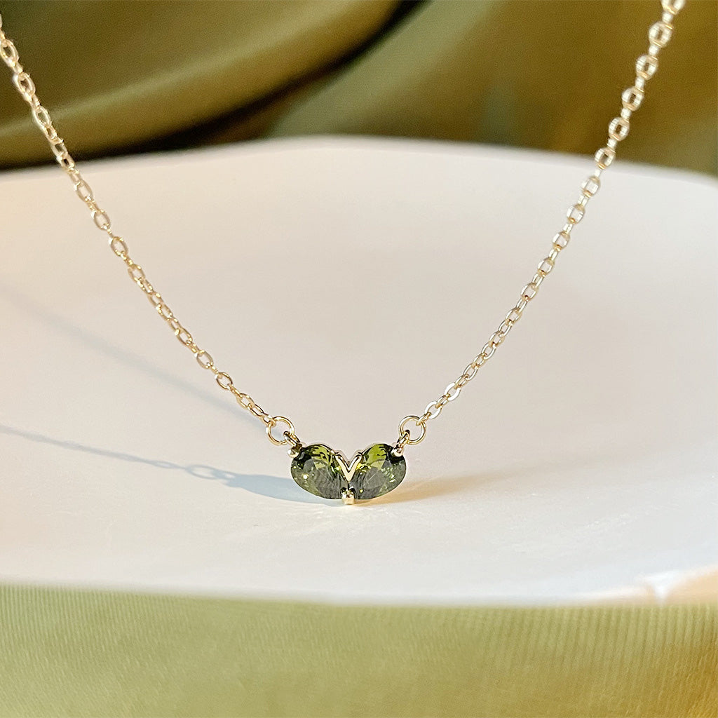 Close-up of a gold-plated choker necklace with a delicate heart-shaped pendant holding two vibrant green emerald gemstones.