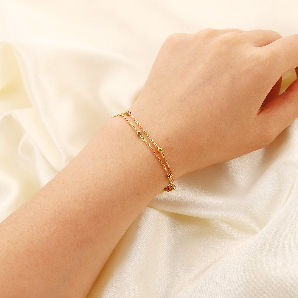 A close-up of the stainless steel double-layered bead bracelet with a heart charm worn on a wrist, showcasing its elegant gold finish.