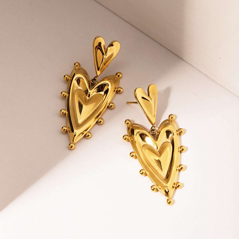 A pair of 18k PVD gold-plated stainless steel earrings featuring a detailed 3D double-heart design with decorative edging.
