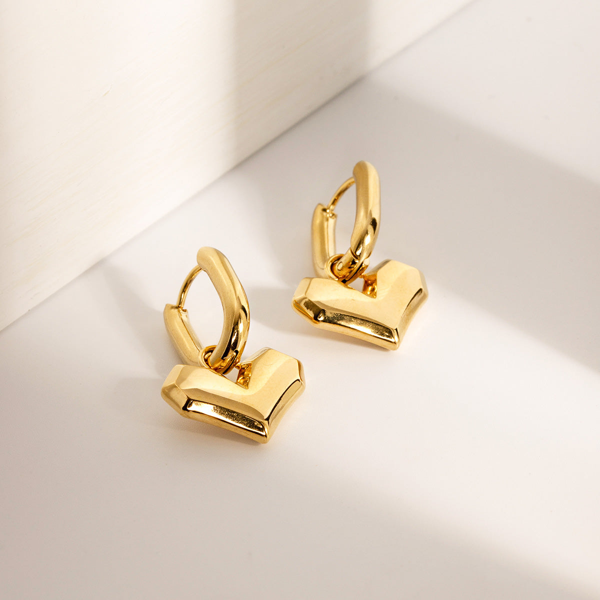 A pair of gold-plated stainless steel heart-shaped hoop huggie earrings, featuring a waterproof and durable hinged design, displayed on a clean background.