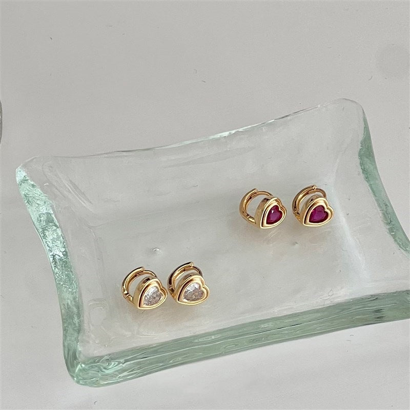 A collection of 18K gold-plated 925 sterling silver huggie earrings, featuring heart-shaped cubic zirconia in both clear and red stones.
