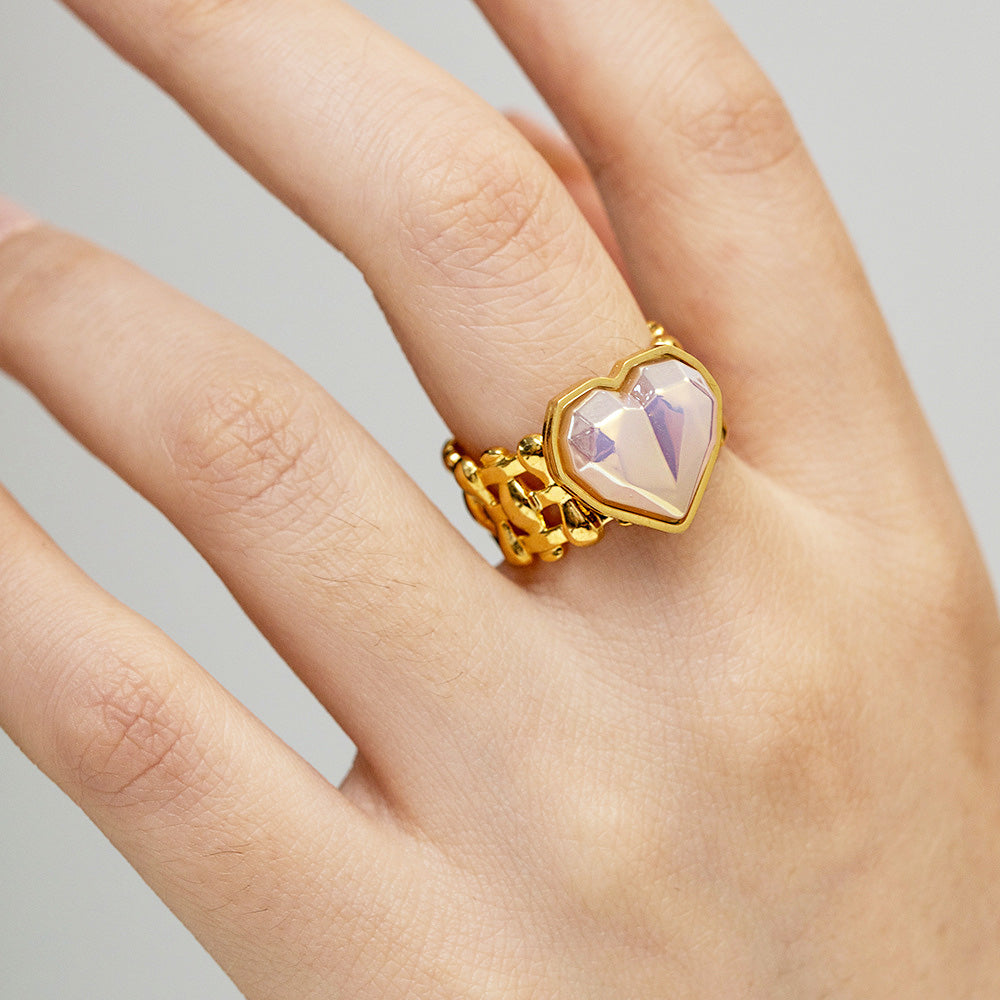 A close-up of a stainless steel, gold-finished open ring from a set of five, featuring a delicate mermaid-style band and a central pale purple heart-shaped gemstone.