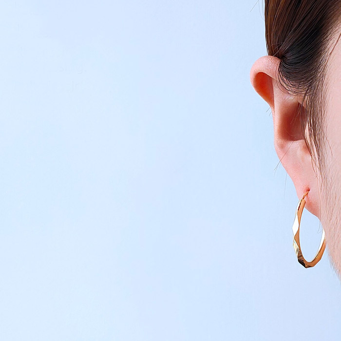 A close-up view of a woman wearing the 28mm Infinity Hoop Earrings, showcasing their elegant gold finish and classic style.