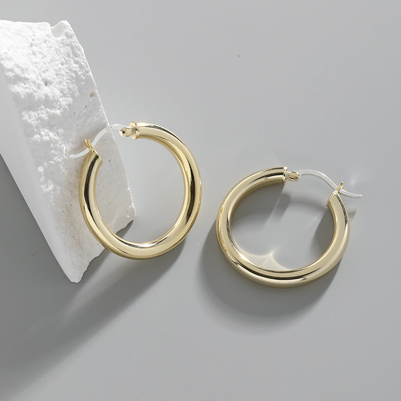 A pair of 18K gold-plated 925 sterling silver small thick hoop earrings displayed on a white stand, showcasing their minimalist and chunky design.