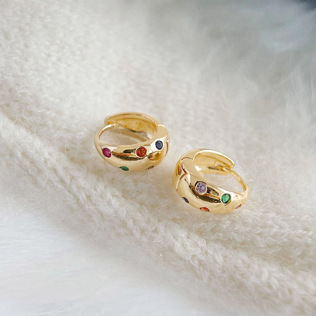 A pair of 14k gold-plated wide hoop earrings with a vibrant array of colorful zircon inlays, displayed against a clean white background.