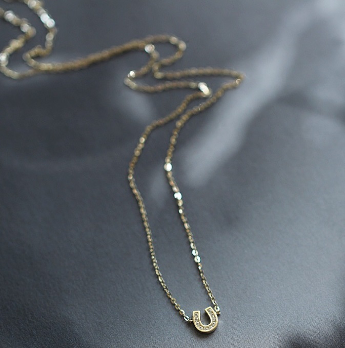 A close-up of a delicate 925 sterling silver horseshoe necklace with a lustrous gold plating, symbolizing good luck.
