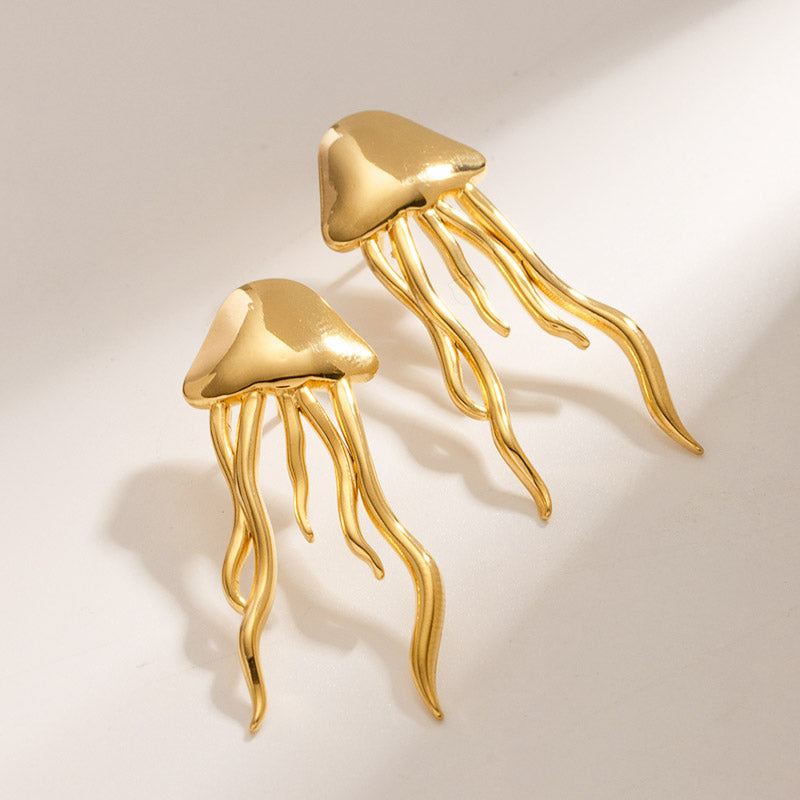 A pair of gold-colored stainless steel jellyfish stud earrings with dome-shaped tops and long wavy tentacles, on a plain background.