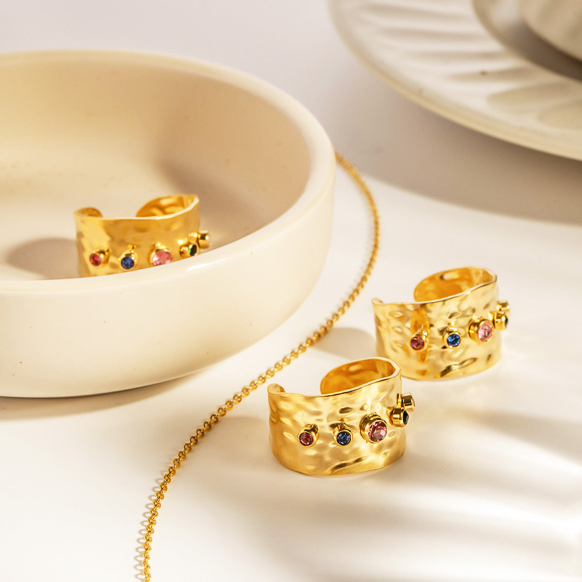 A set of five stainless steel hammered cuff rings with colorful cubic zirconia gemstones, displayed on a white surface.