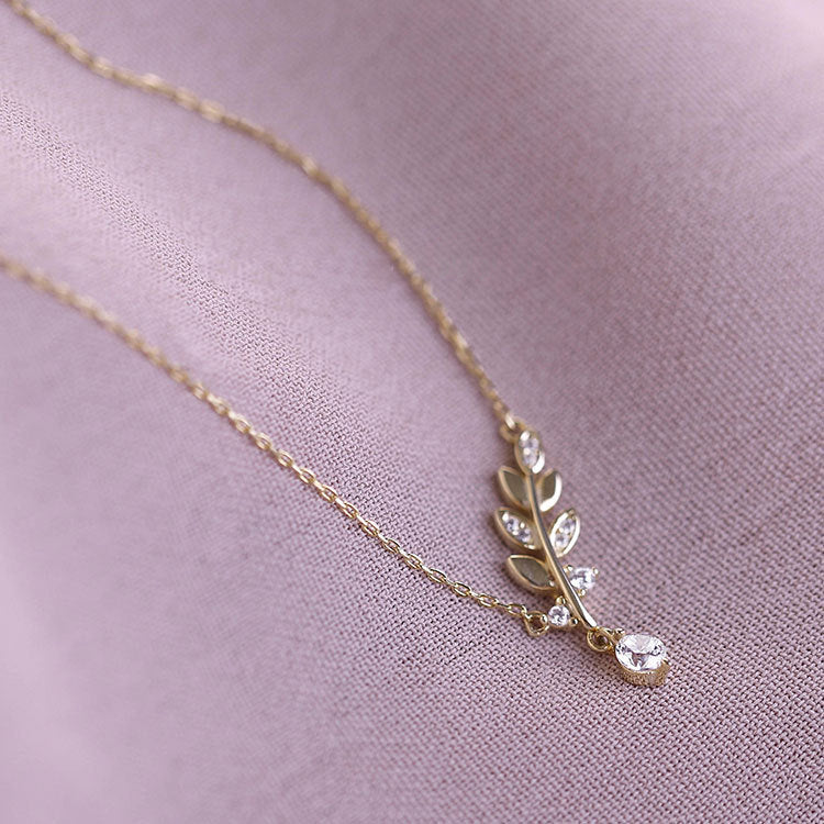 A close-up of the 925 sterling silver delicate small CZ leaf necklace in a radiant gold finish, showcasing the sparkling cubic zirconia stones on the leaf pendant.