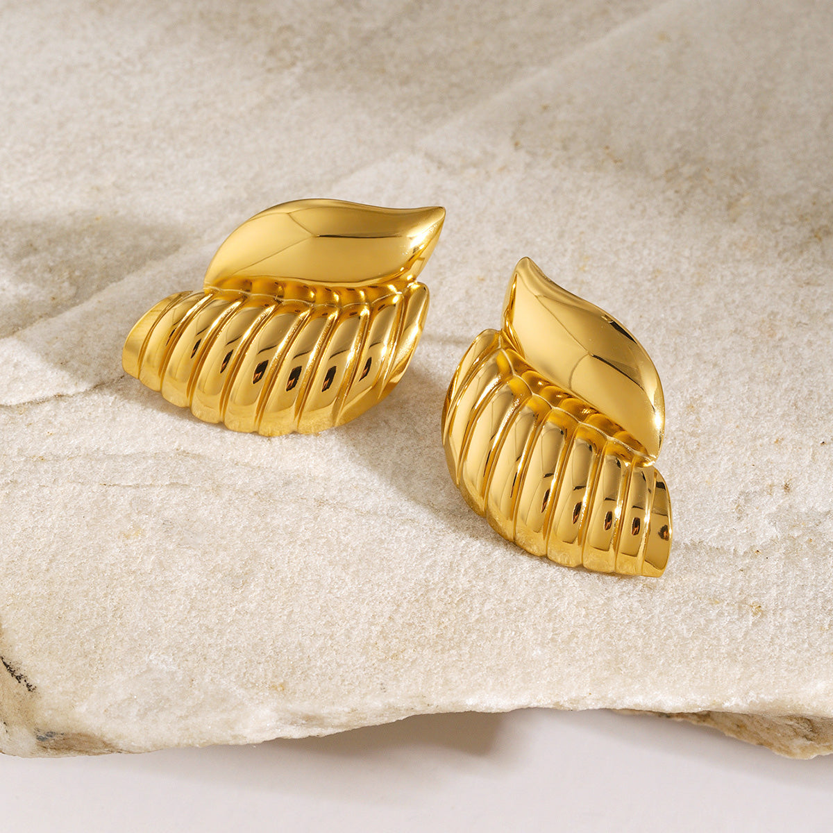 A pair of gold-tone conch shell stud earrings made from waterproof stainless steel, displayed against a clean white background.